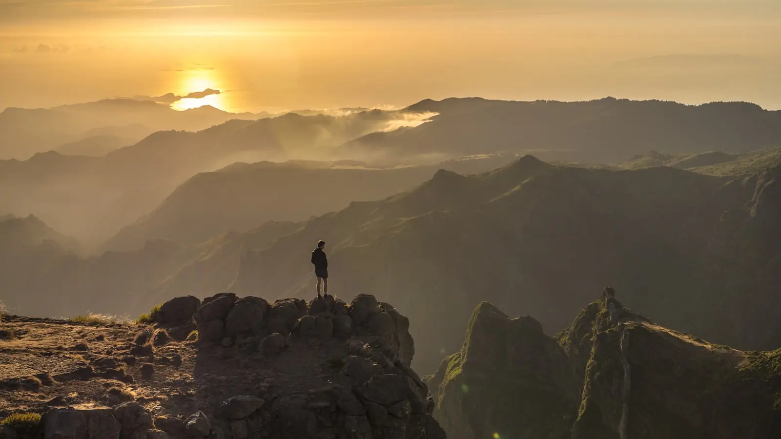 Silhouette eines Menschen auf einem Berggipfel im warmen Licht der goldenen Stunde.